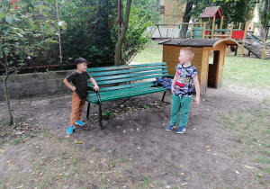 Przemek razem z Alimem stoją w ogródku przedszkolnym przy ławce